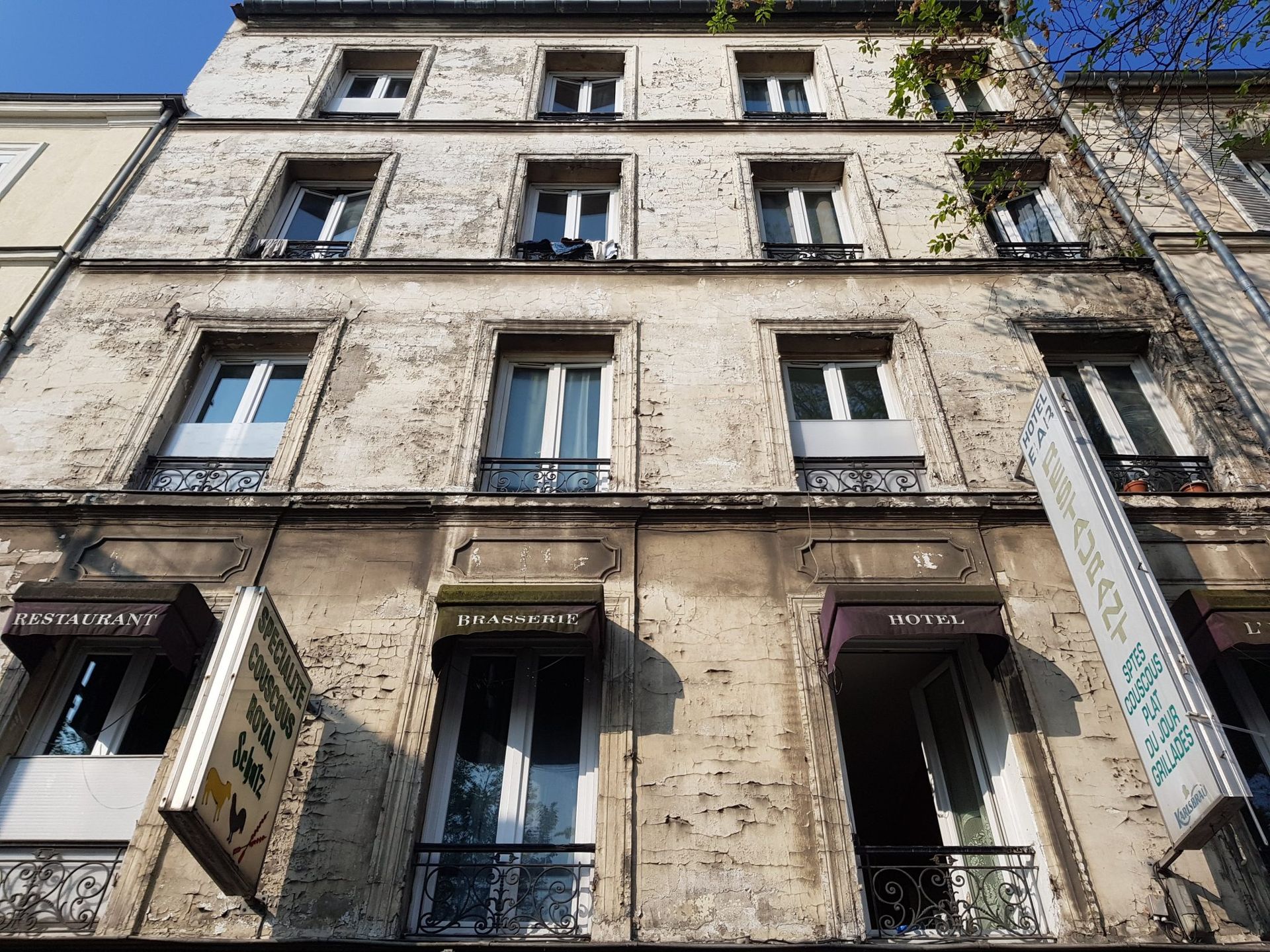 Vue de la façade beige d'un immeuble à Paris, avec ses nombreuses fenêtres et ses commerces au rez-de-chaussée.