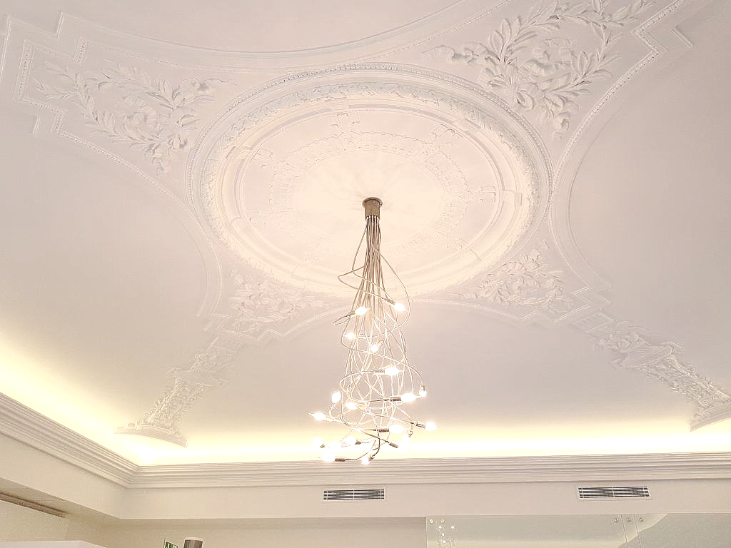 Un délicat lustre en cristal est suspendu à un plafond orné de moulures en plâtre blanc.