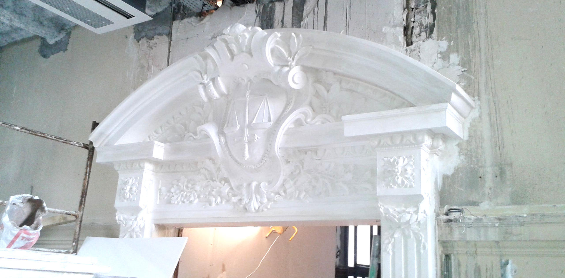 Une arche ou un manteau de cheminée orné de sculptures complexes en plâtre blanc, au-dessus d'une porte inachevée.