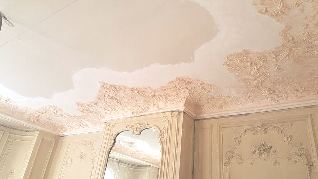 Un coin de pièce orné, dans des tons beiges, avec des moulures décoratives complexes au plafond et aux murs.