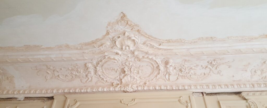 Moulures décoratives en plâtre couleur crème, finement travaillées, ornant un plafond et présentant des motifs floraux.