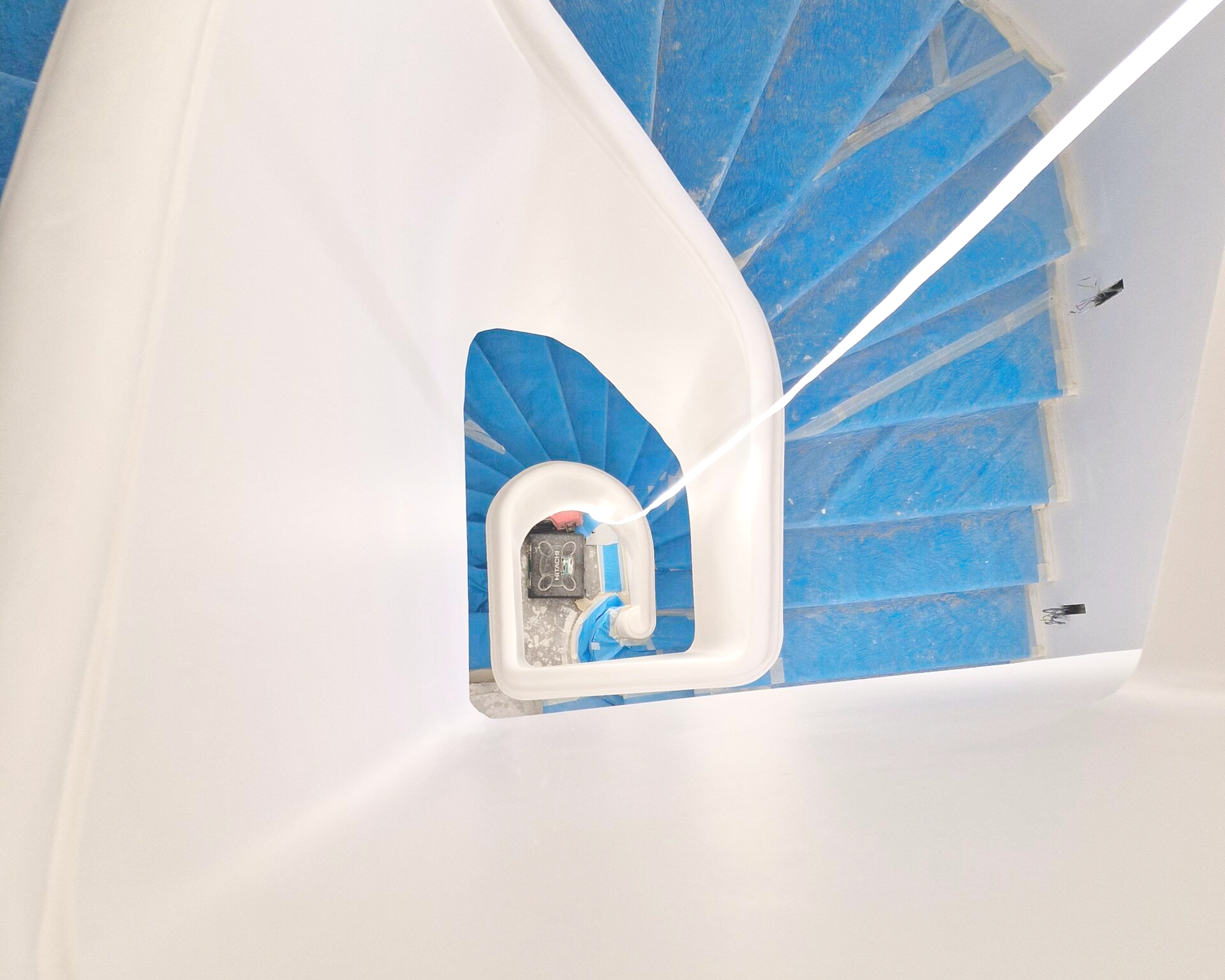 Vue en plongée d'un escalier en colimaçon d'un blanc éclatant, aux marches d'un bleu vif, menant à un petit palier central.