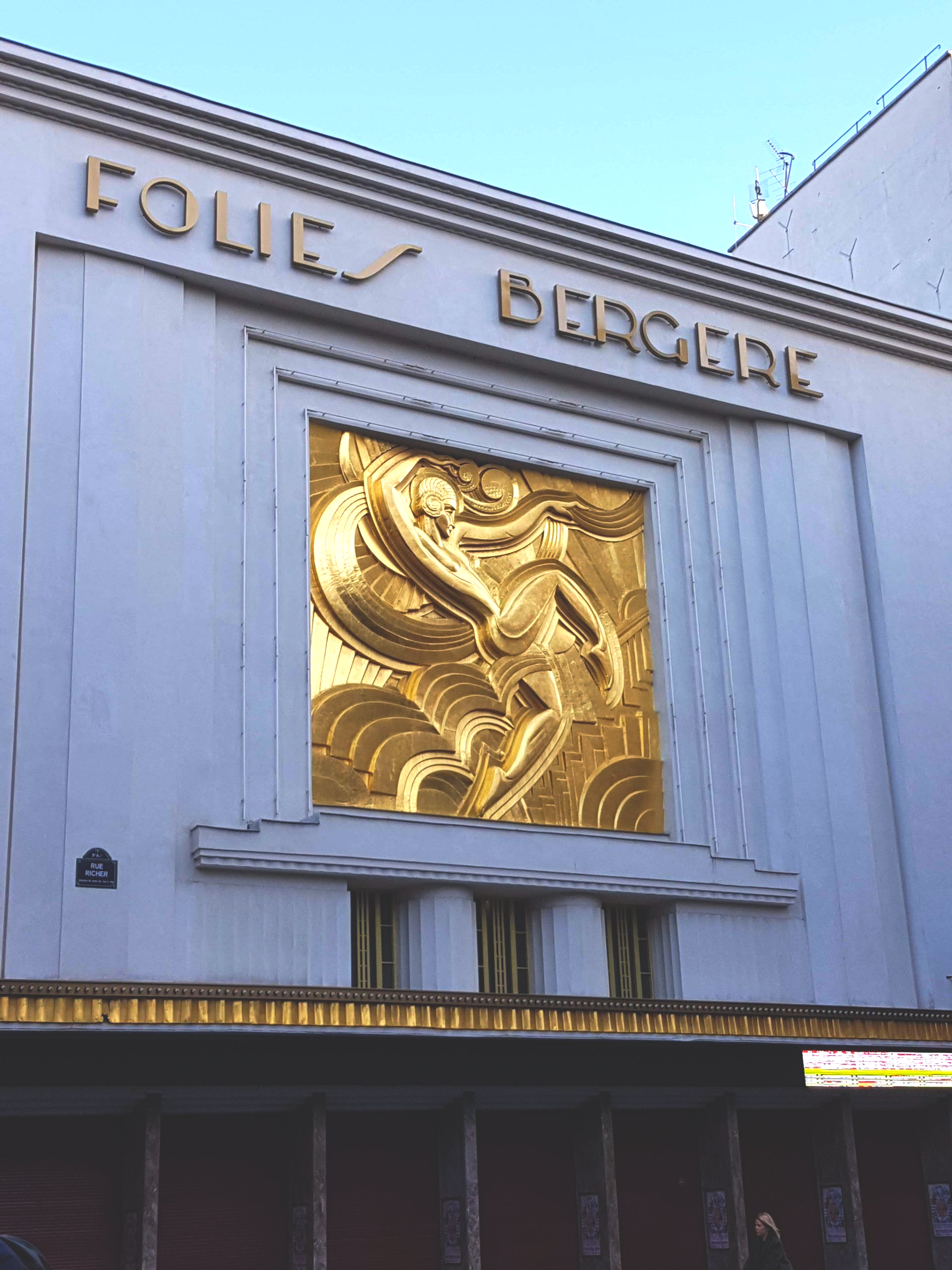 La façade couleur crème des Folies Bergère, ornée d'une grande sculpture en relief recouverte de feuilles d'or.