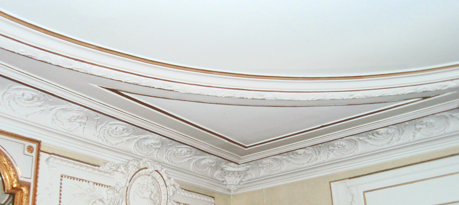 Moulure de plafond blanche ornée de détails en feuille d'or dans un coin d'une pièce de style classique.
