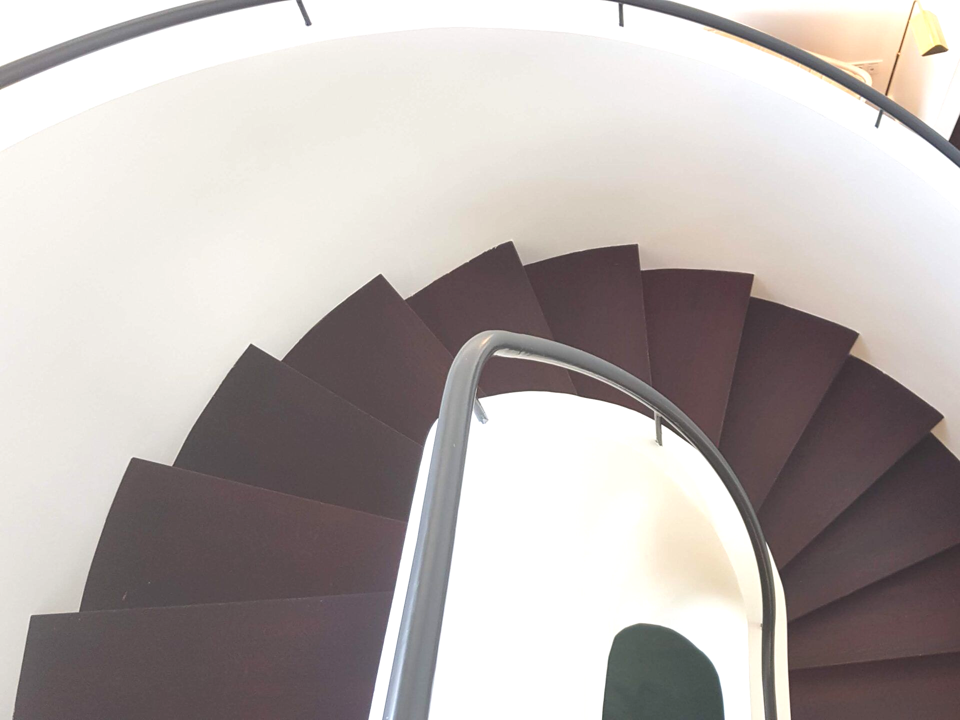 Vue en plongée d'un escalier en colimaçon moderne avec des marches recouvertes de moquette marron foncé, des murs blancs.