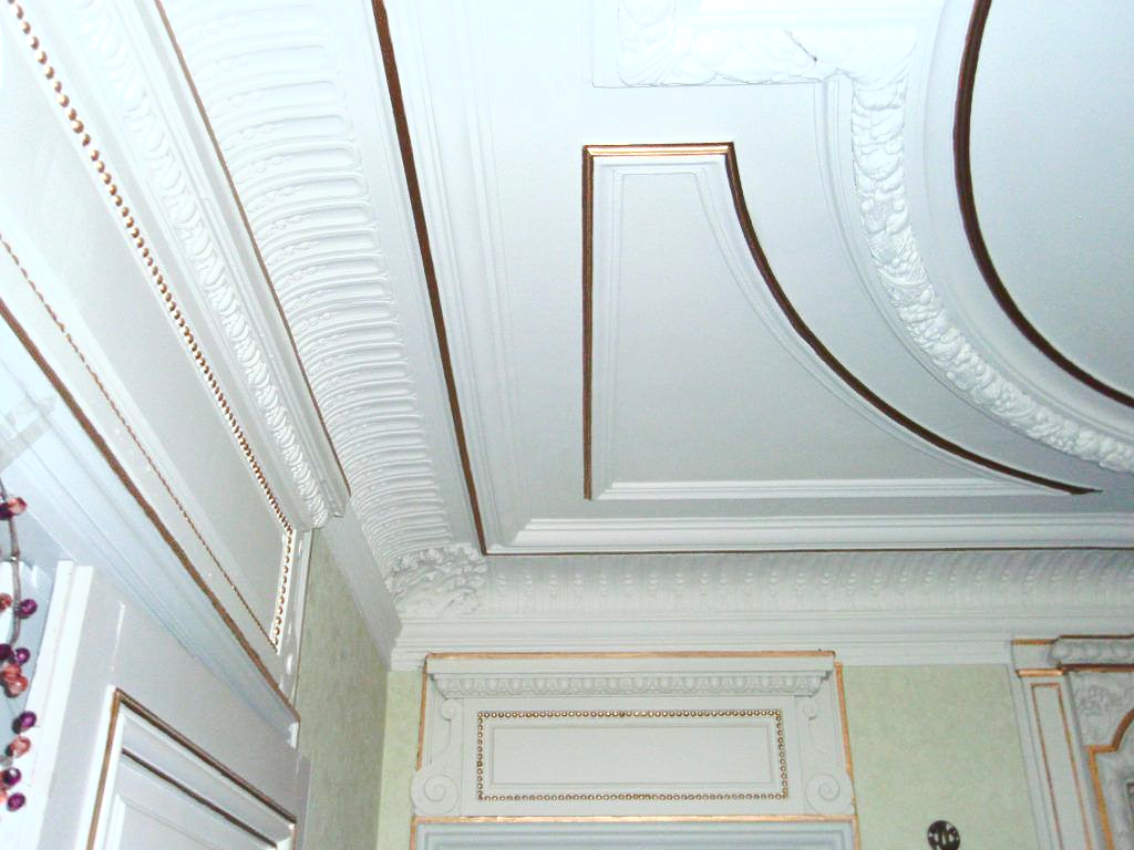 Un plafond blanc finement travaillé, orné de moulures et de panneaux architecturaux.
