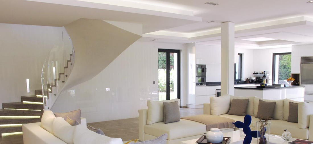 Salon moderne blanc avec un escalier sculptural, un éclairage intégré et un canapé modulable blanc.