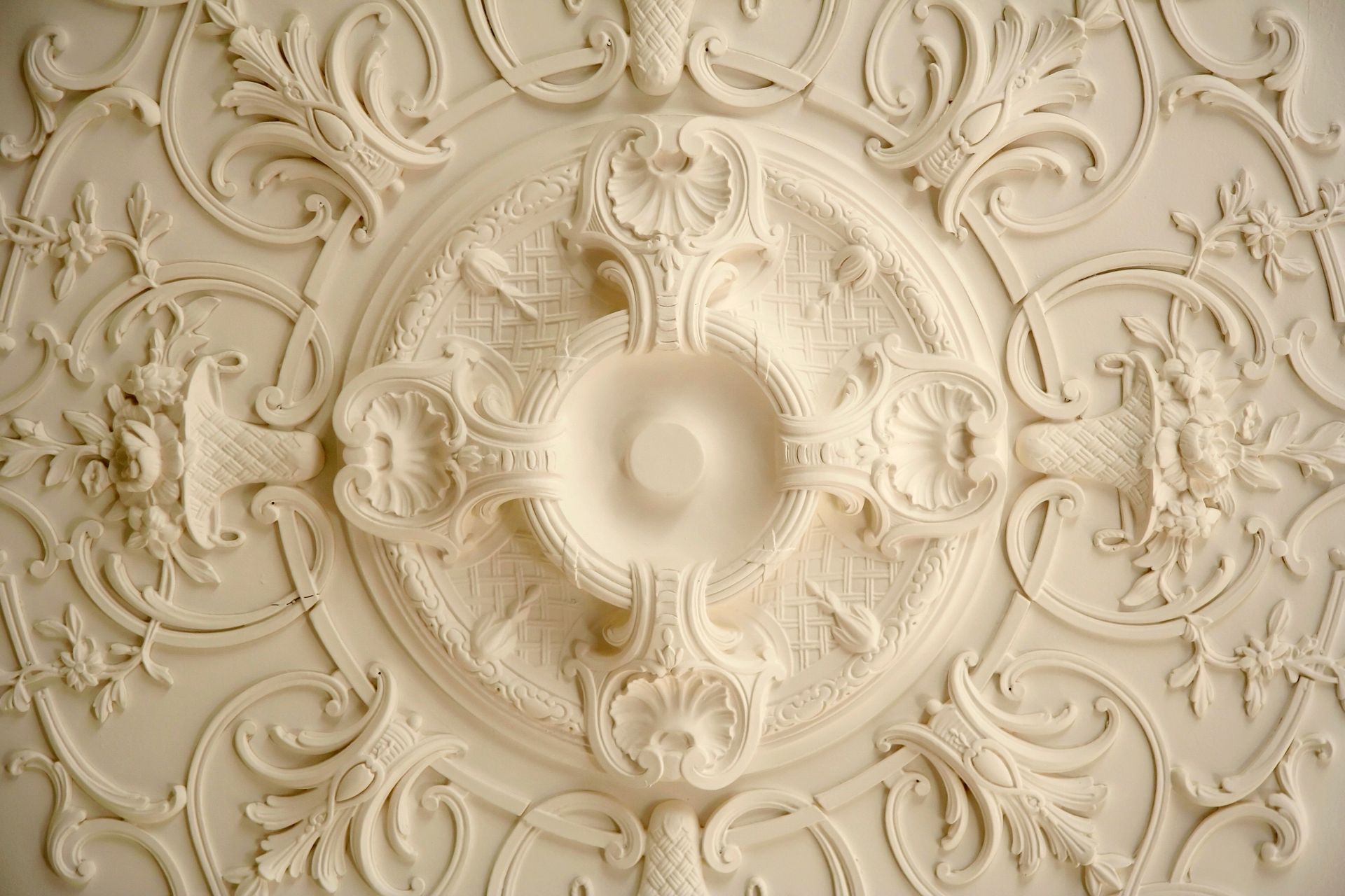 Médaillon de plafond en plâtre couleur crème, finement détaillé, orné de motifs floraux et de volutes disposés en cercle.