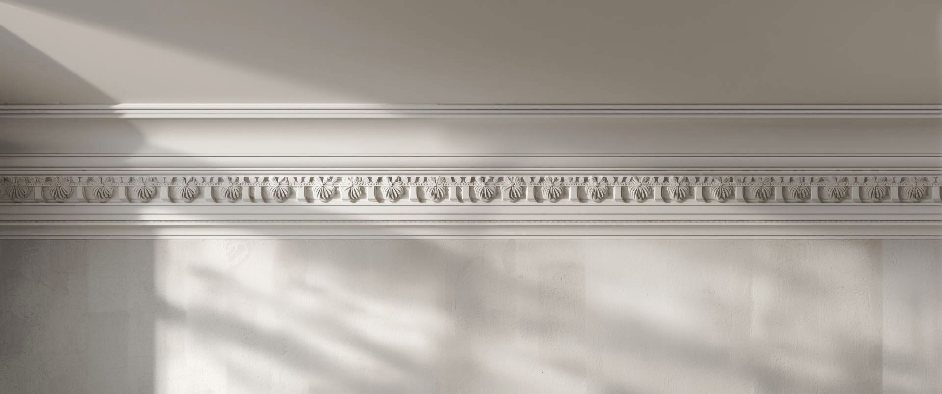 Un mur couleur crème orné de moulures complexes à motifs floraux en relief, éclairé par de douces ombres.