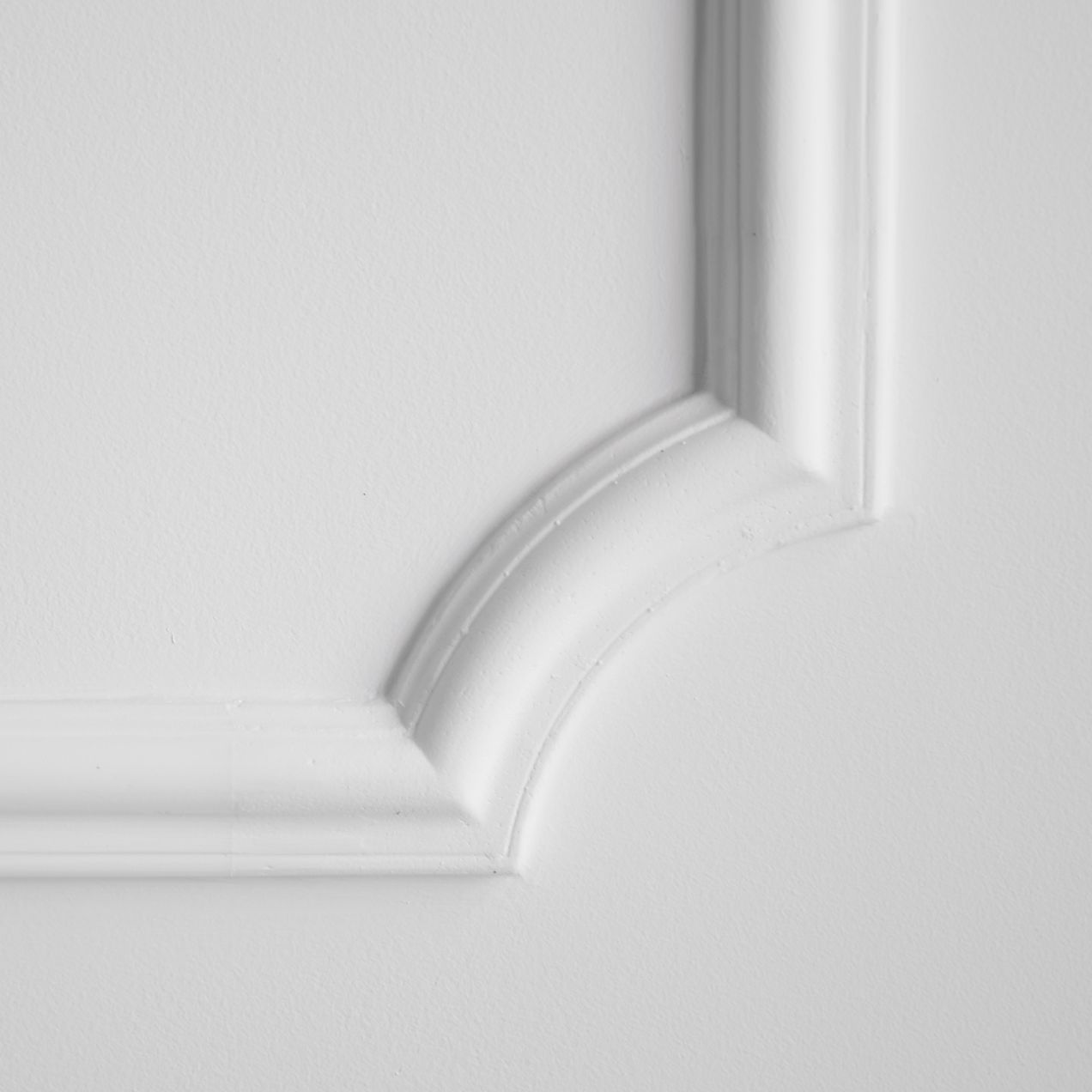 Un coin de moulure murale décorative blanche avec un détail de design incurvé sur un fond blanc uni.