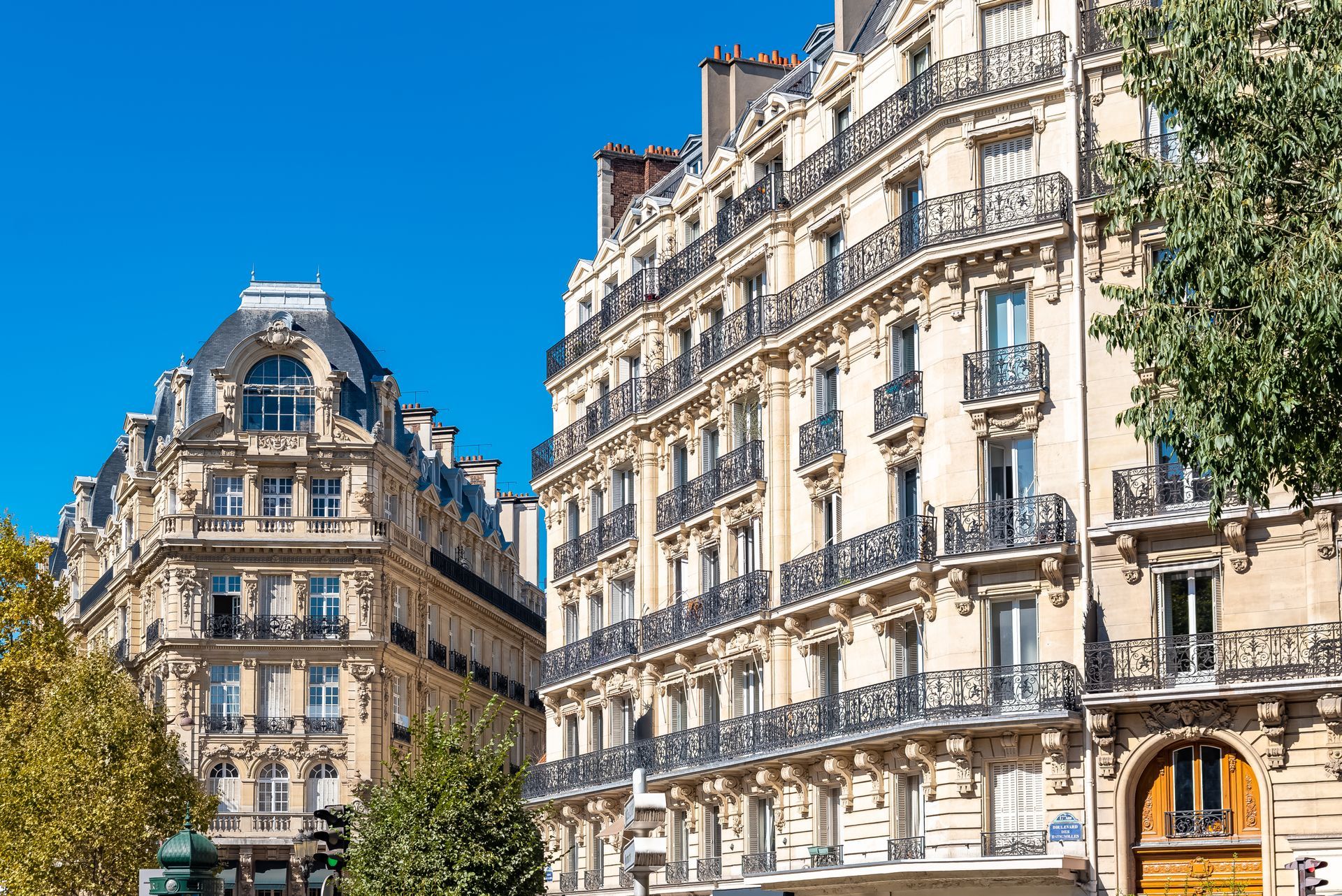 D'élégants immeubles beiges de style parisien, avec des balcons noirs ouvragés et une architecture en pierre.