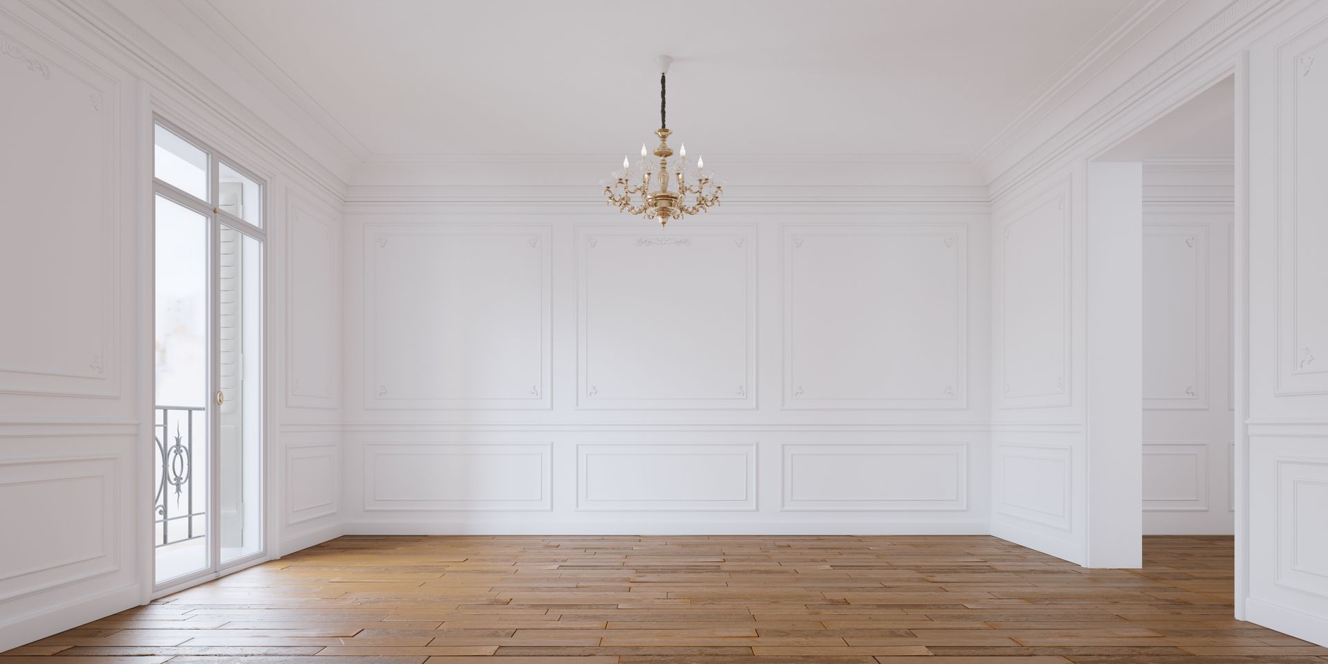 Une pièce lumineuse et vide, aux murs lambrissés blancs, avec un lustre et un parquet et une porte vitrée.