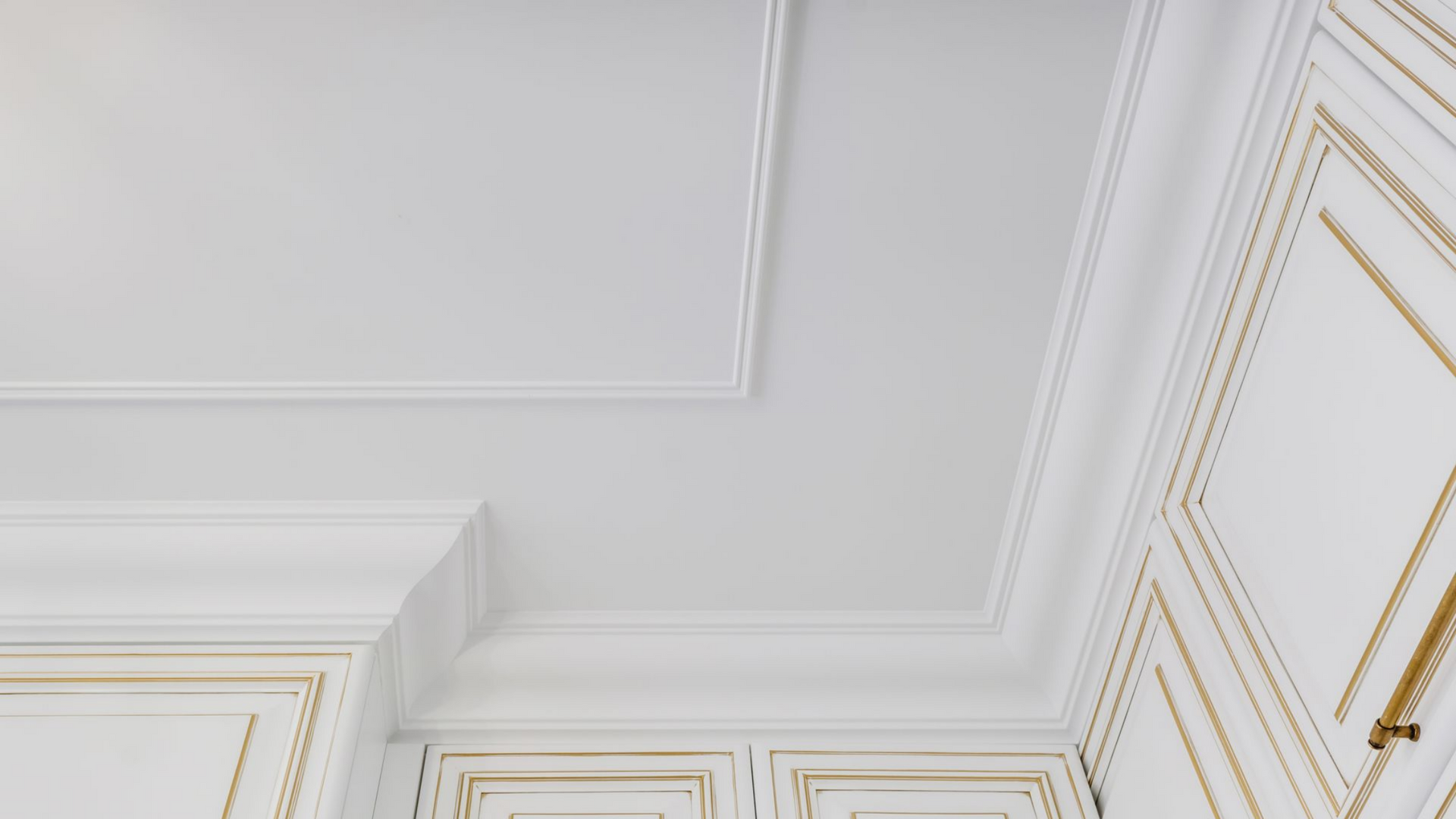 Un plafond blanc orné de moulures décoratives et d'un panneau rectangulaire encastré, encadré par des meubles blanc cassé.