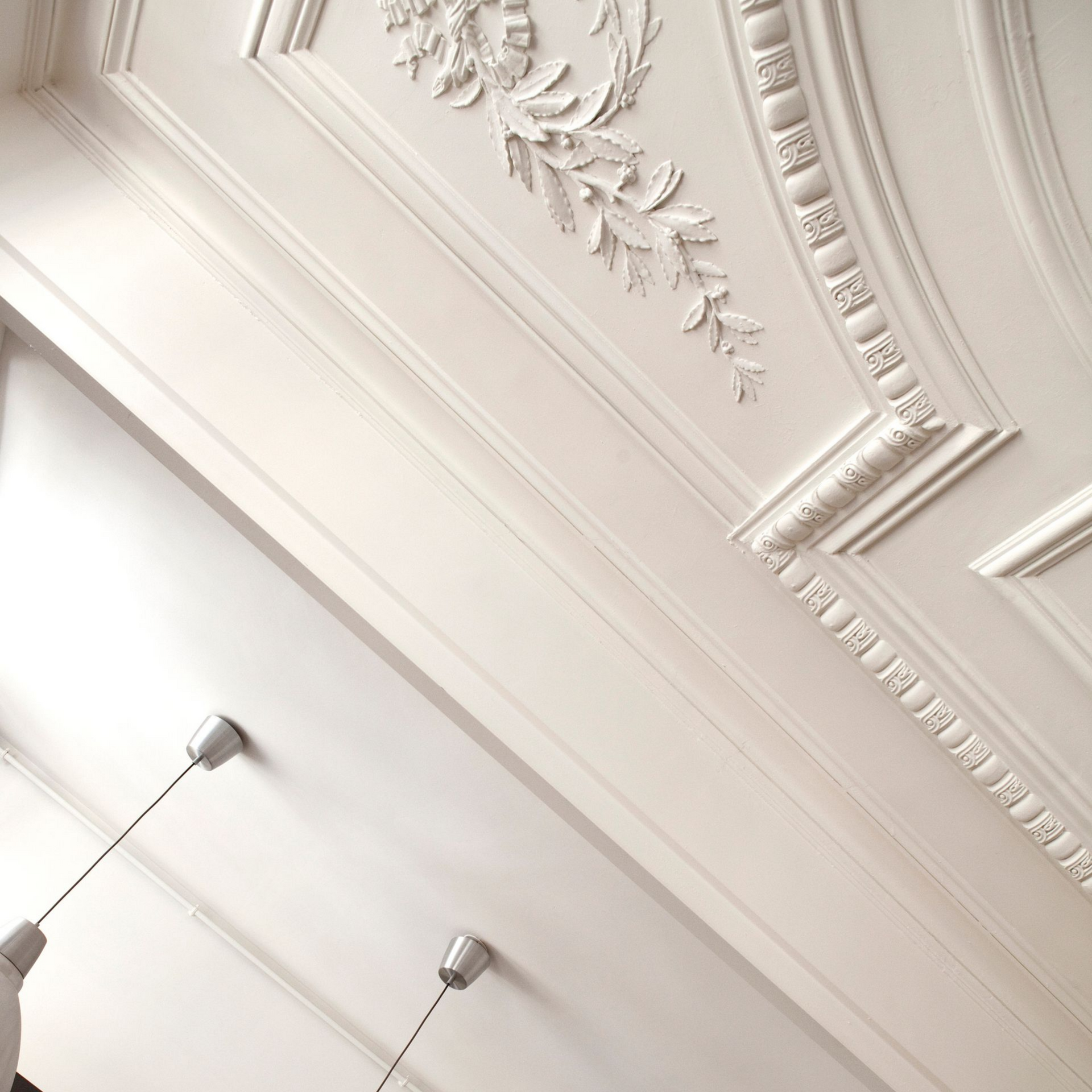Un plafond blanc orné de moulures florales classiques, surmonté de deux petites suspensions argentées.