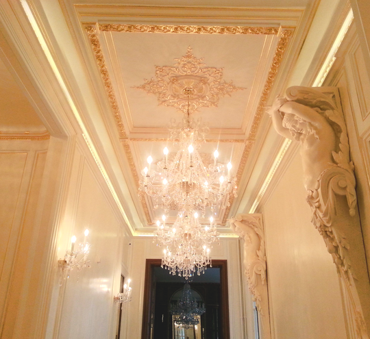 Un grand hall d'entrée orné d'un lustre en cristal, de détails de plafond richement décorés de dorures.