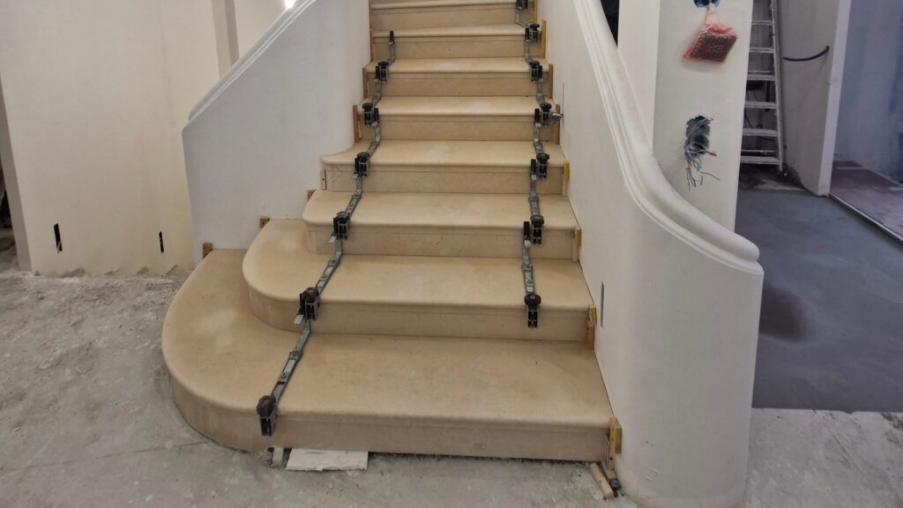 Un escalier en construction, des pinces métalliques maintenant les marches en place sur un escalier en bois clair et incurvé.