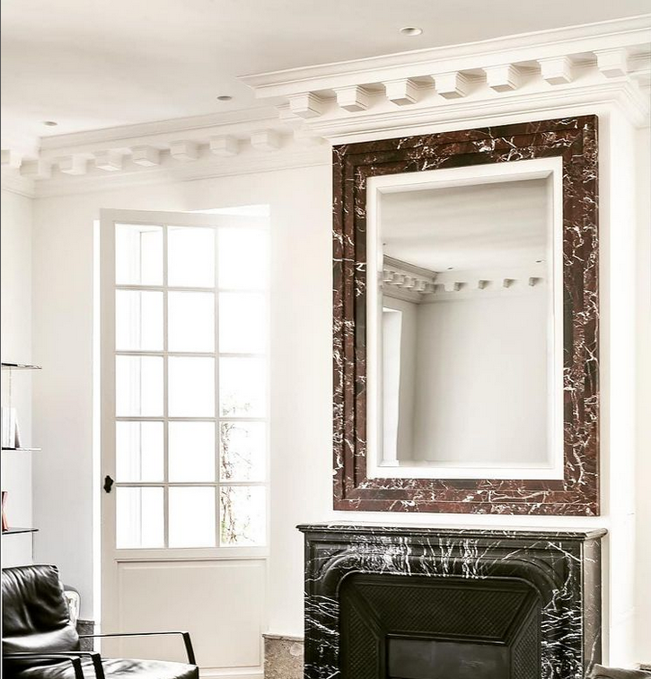 Une cheminée en marbre sombre, surmontée d'un miroir assorti, dans une pièce lumineuse aux murs blancs.