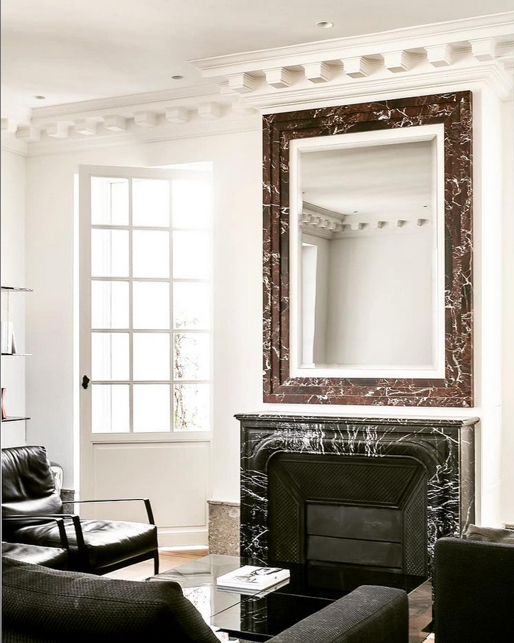 Dans une pièce lumineuse, une cheminée en marbre noir surmontée d'un miroir assorti.