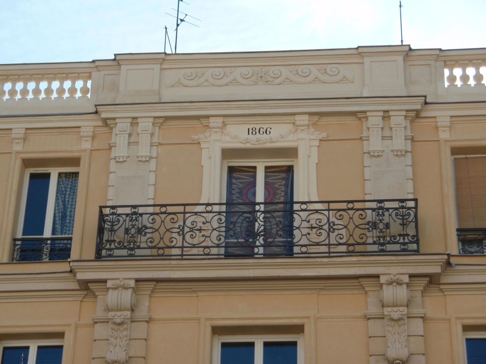 Façade d'immeuble couleur crème avec un balcon central, des sculptures en pierre ornementales.