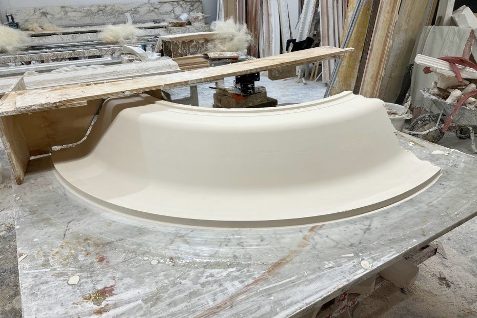 Une moulure incurvée en plâtre ou en pierre de couleur claire repose sur un établi dans un atelier.