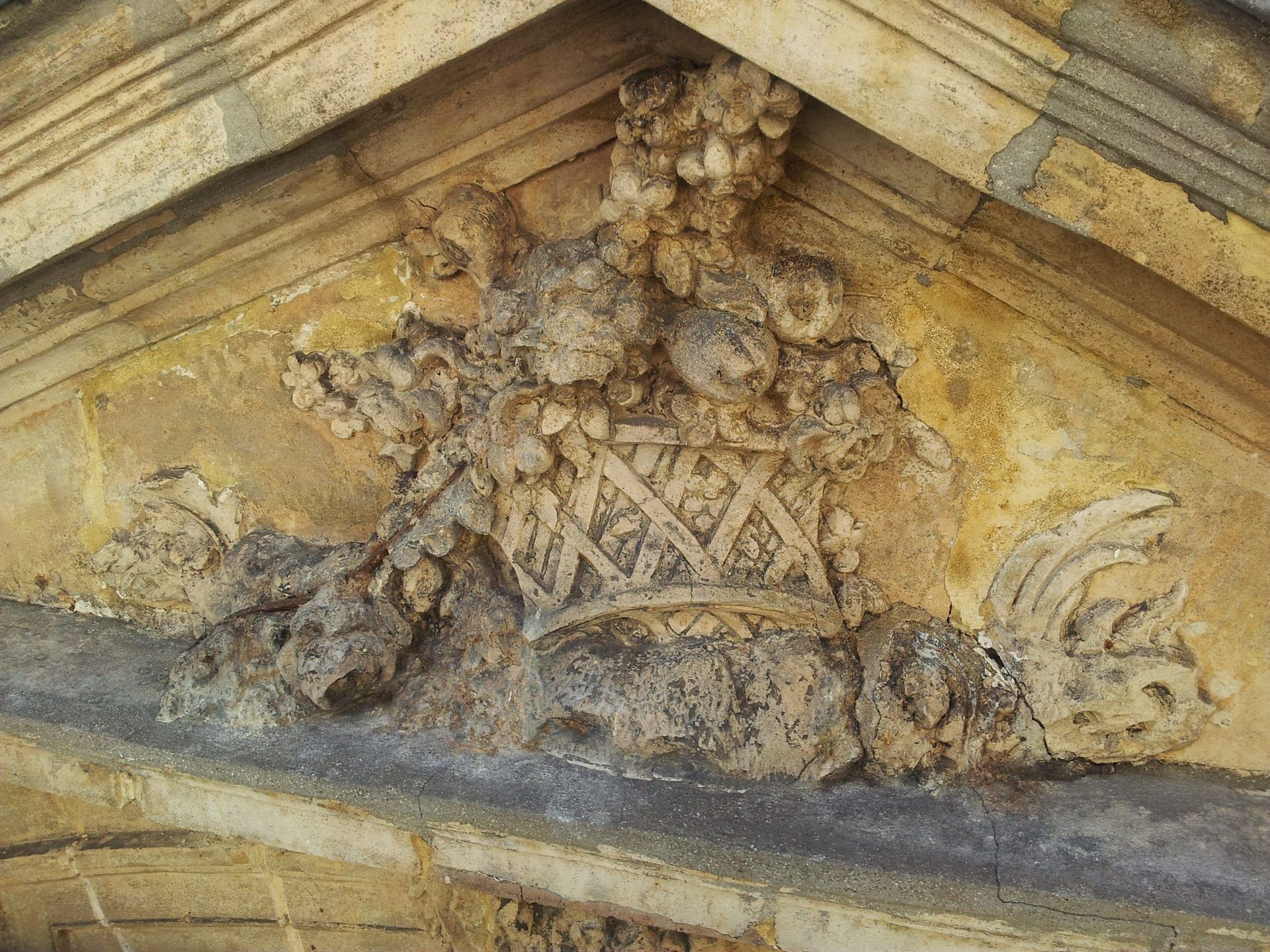 Relief en pierre dans un fronton triangulaire représentant un panier rempli de fruits sculpté dans du calcaire beige.