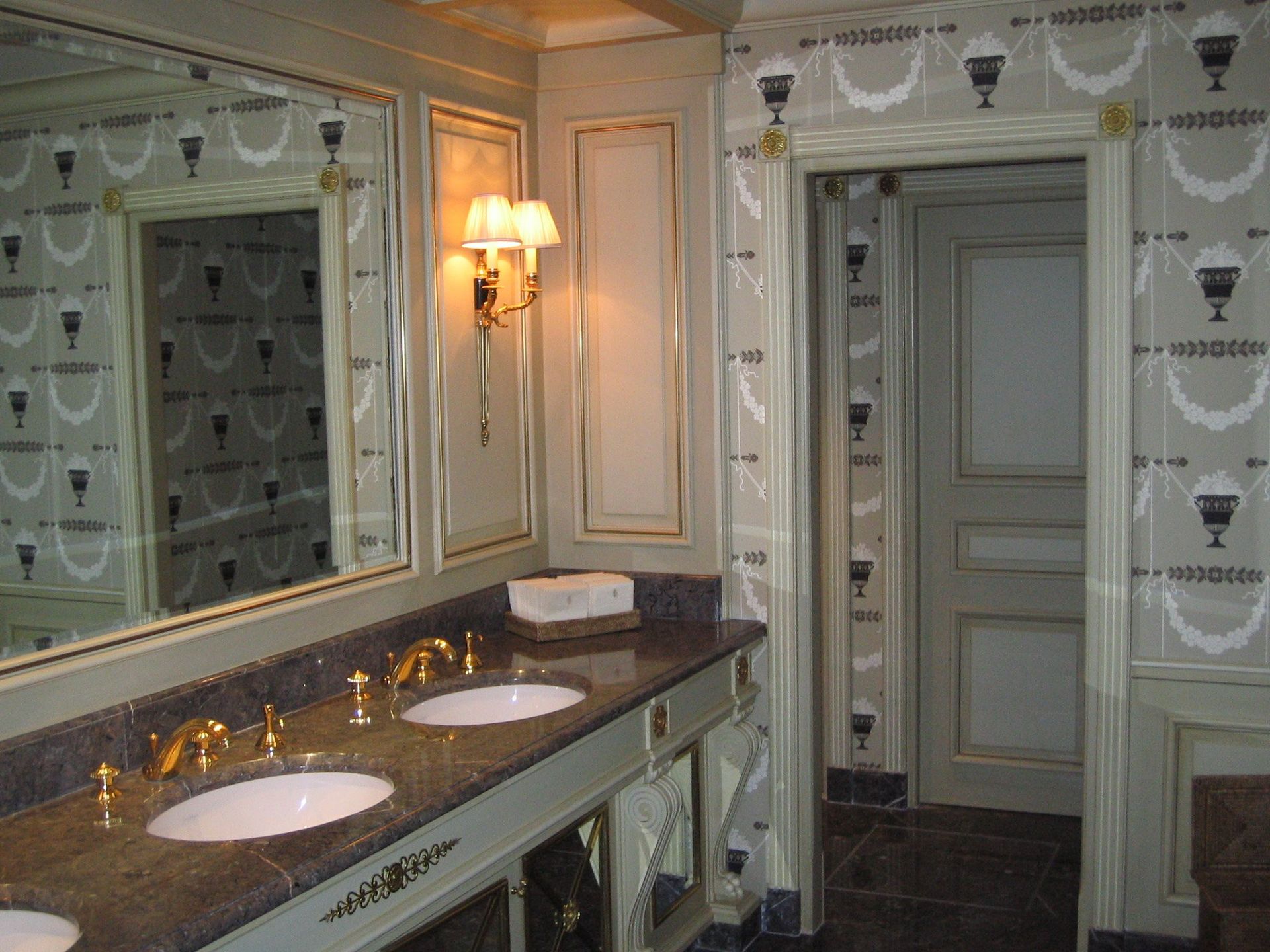 Une double vasque en marbre dans une salle de bains beige de style classique, avec du papier peint à motifs.