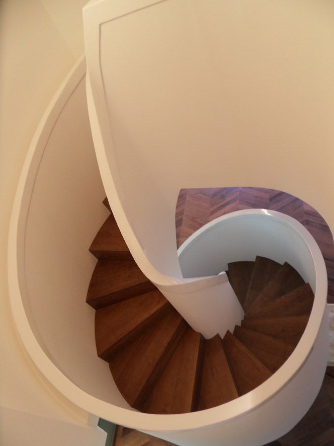 Un escalier en colimaçon aux marches en bois sombre et au mur incurvé blanc, vu d'en haut.