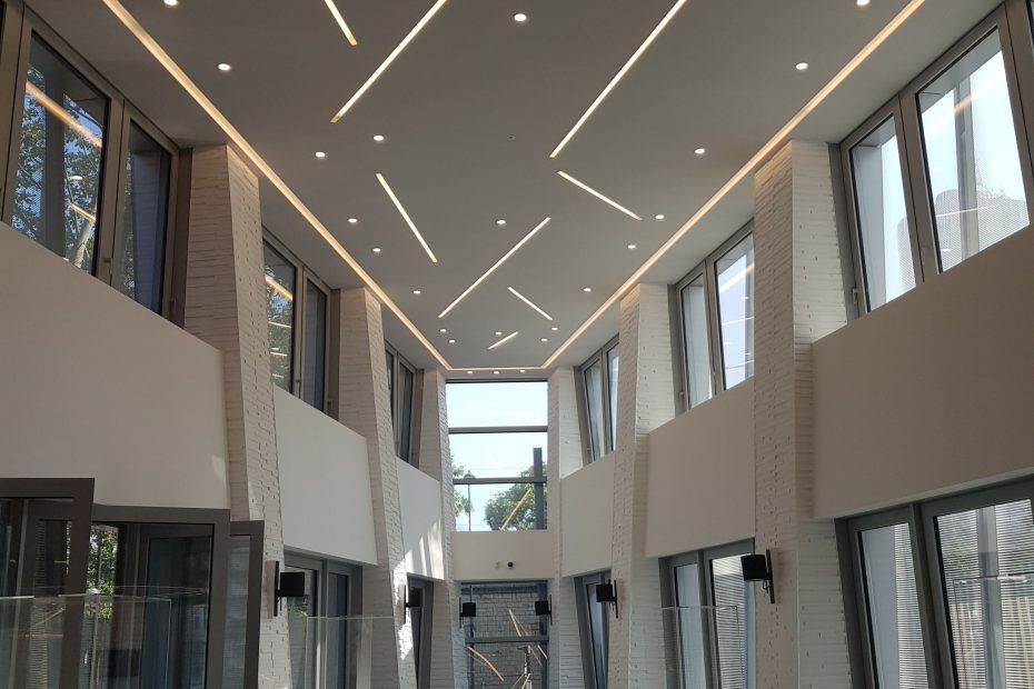 Une pièce, avec de hauts murs, de grandes fenêtres et un plafond blanc orné de bandes lumineuses.