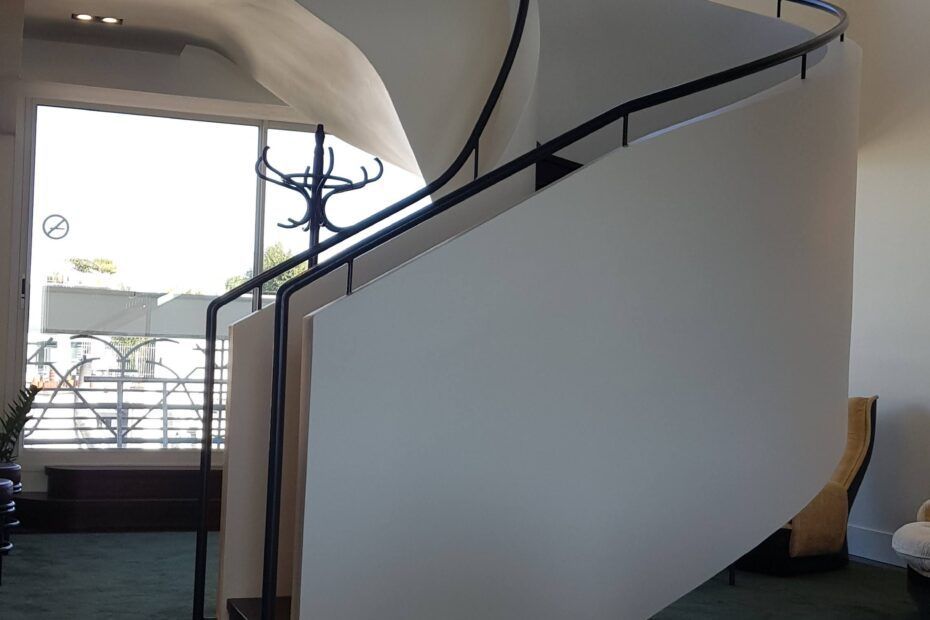 Un escalier blanc incurvé avec une rampe en métal noir à l'intérieur d'un bâtiment.