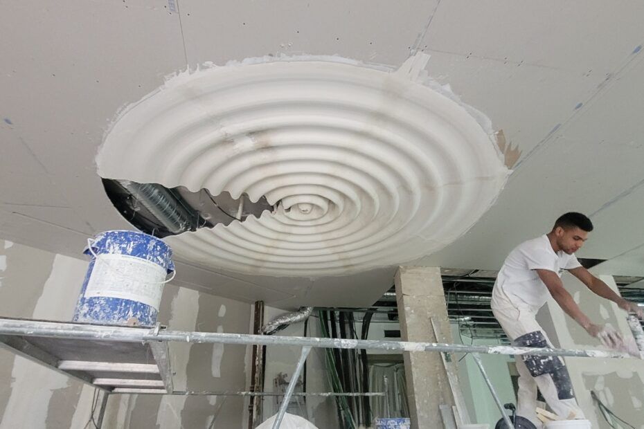 Une personne travaille sur un élément architectural composé de cercles concentriques au plafond d'un chantier en activité.