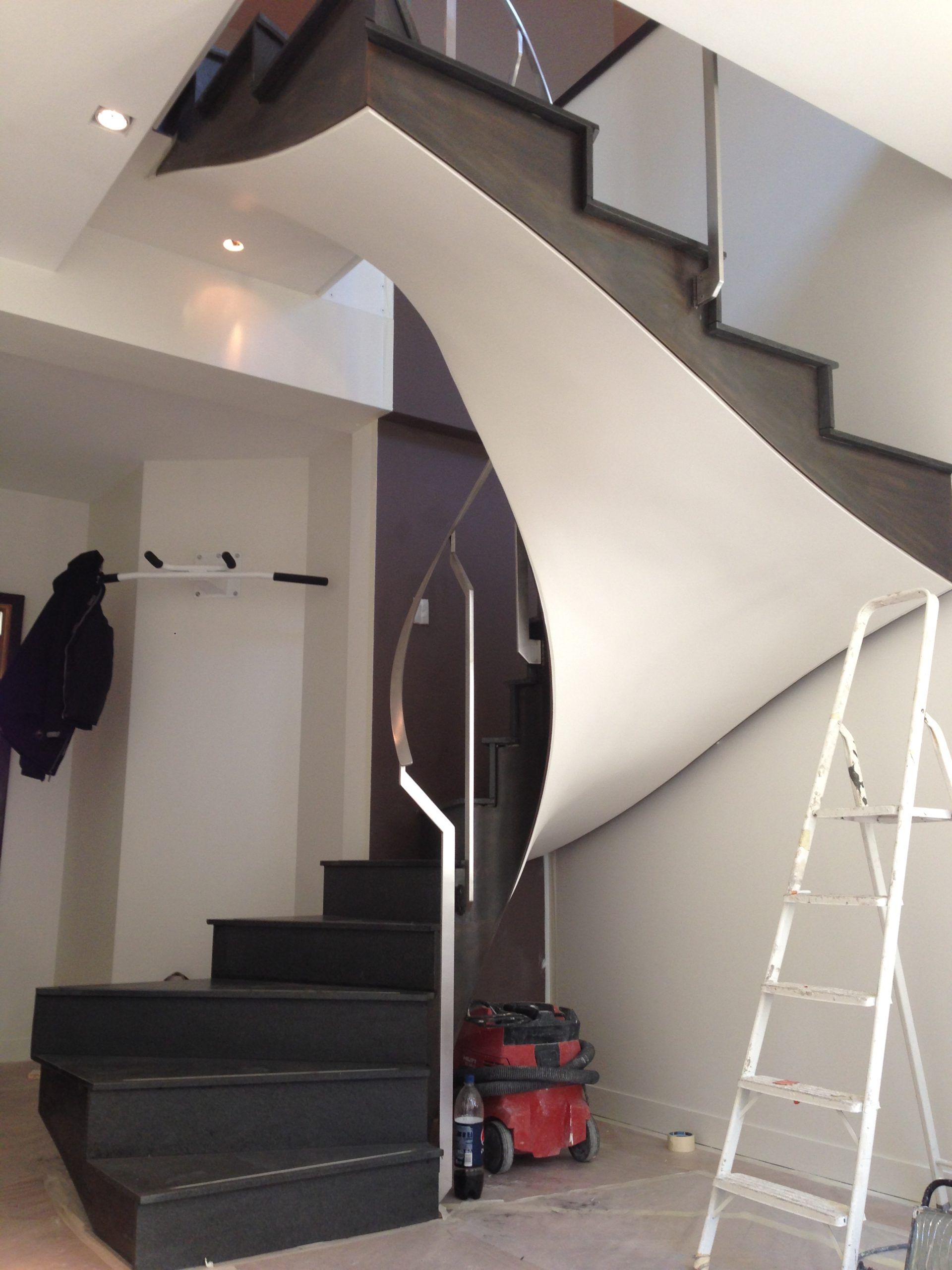 Un escalier moderne avec des marches en pierre noire, une partie inférieure incurvée blanche et une rampe en verre.