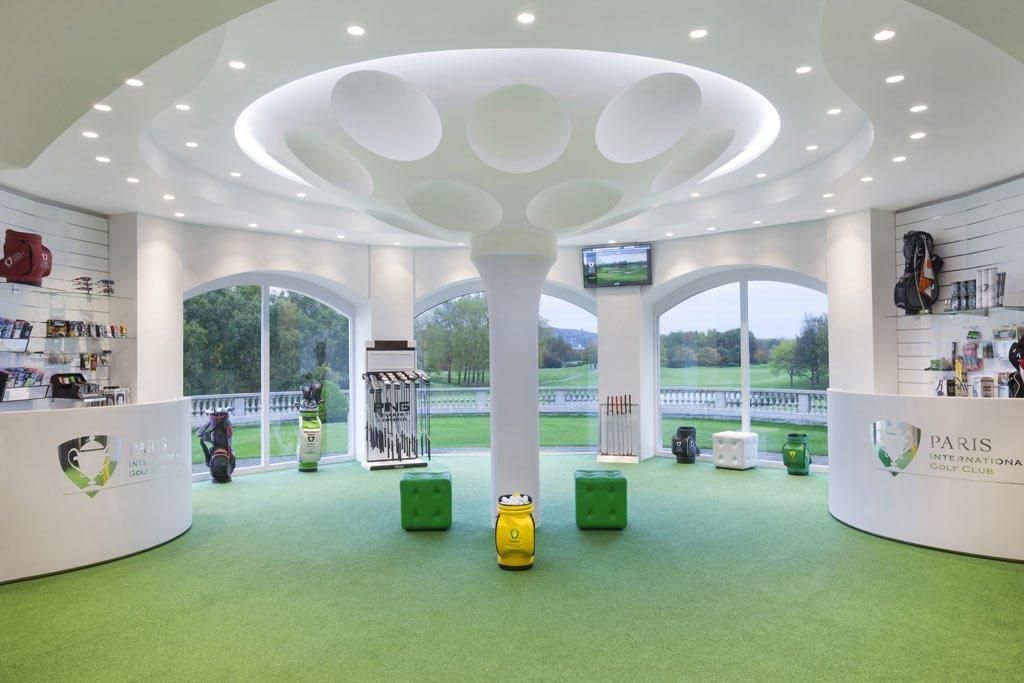 Une boutique de golf circulaire avec un sol en gazon artificiel, des comptoirs blancs et une colonne centrale.