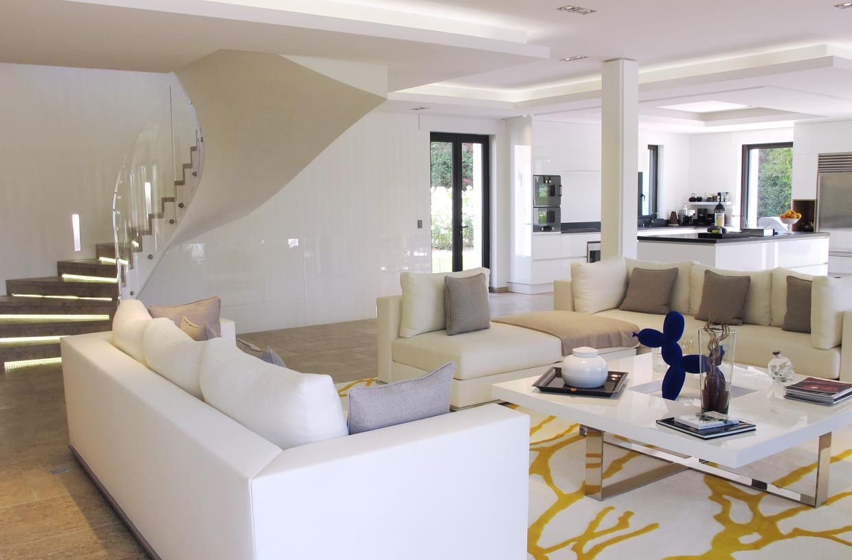 Un salon spacieux et moderne, blanc, avec un escalier incurvé, des canapés d'angle et un tapis à motifs.