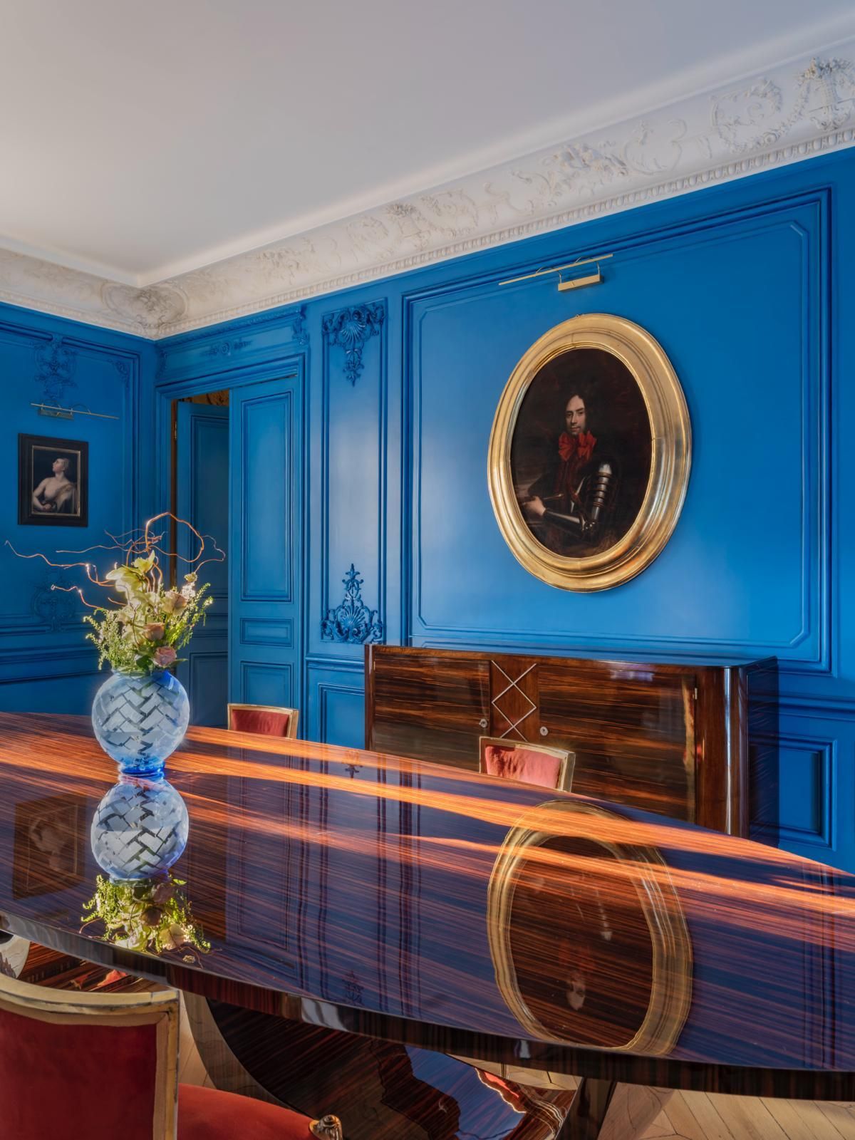 Une salle à manger avec des murs lambrissés d'un bleu éclatant, une table en bois foncé.