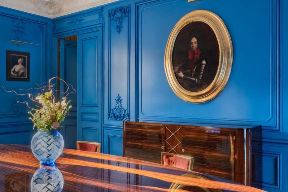 Un portrait dans un cadre ovale doré est accroché sur un mur lambrissé d'un bleu éclatant.