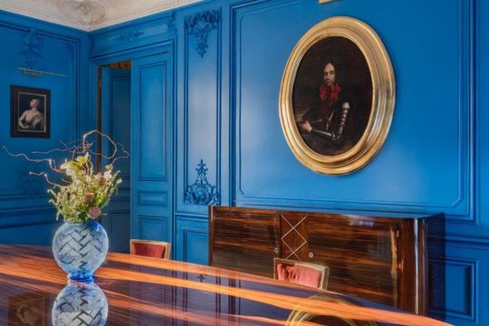 Une pièce d'un bleu éclatant présente un grand cadre ovale doré, au-dessus d'un buffet en bois poli.