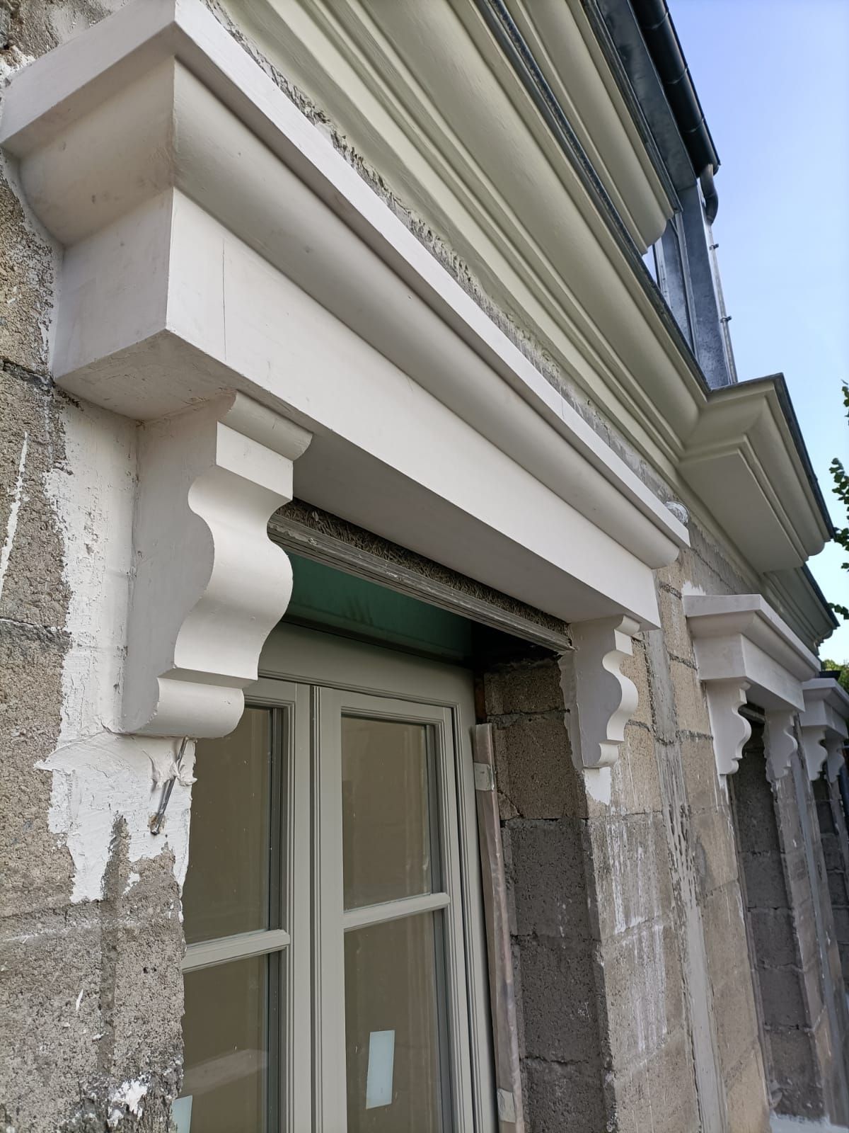 Moulure décorative en pierre blanche, soutenus par des consoles sculptées, sur un mur extérieur en maçonnerie.