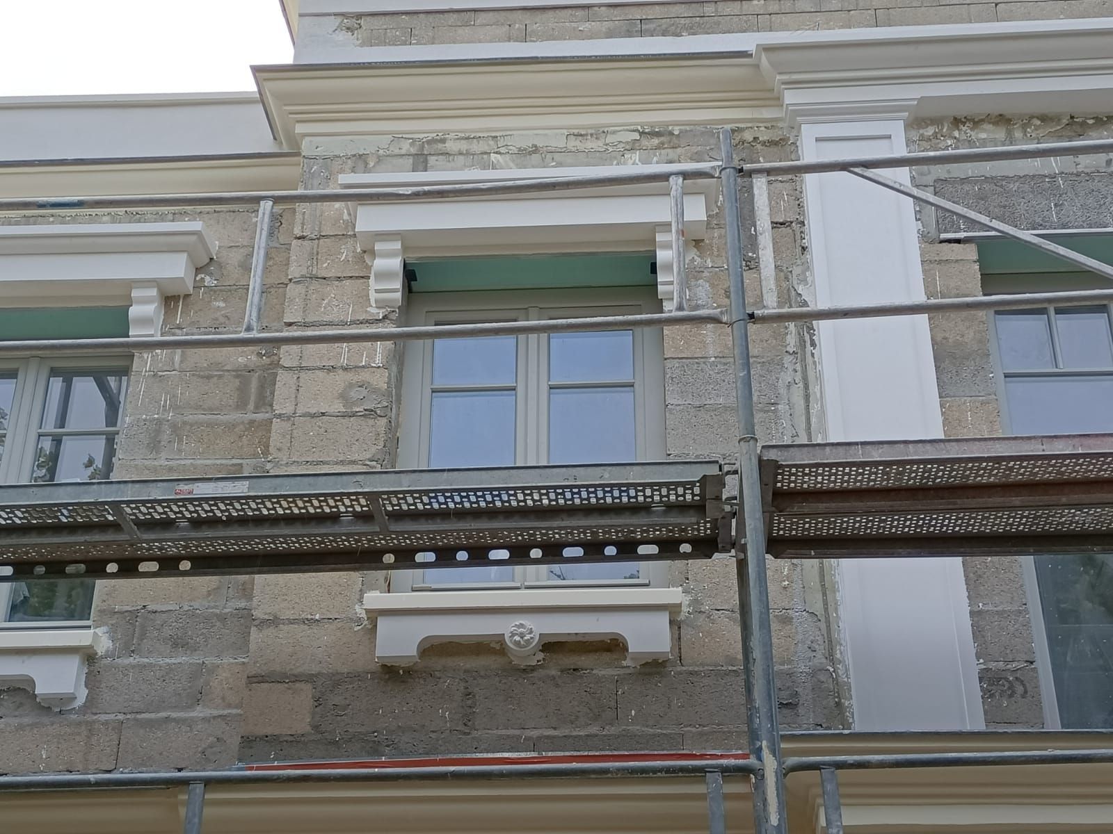 Façade en pierre d'un bâtiment en rénovation, avec des fenêtres ornées de moulures architecturales décoratives.