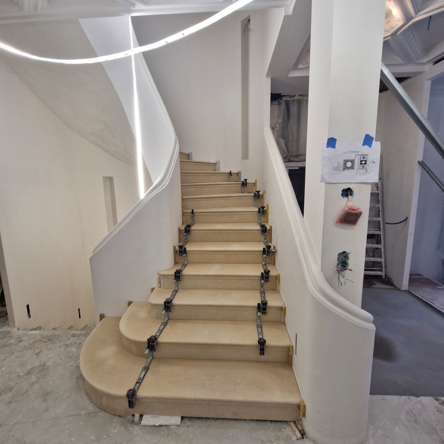 Un escalier courbe en construction, avec des protections en bois sur les marches et des fixations temporaires.