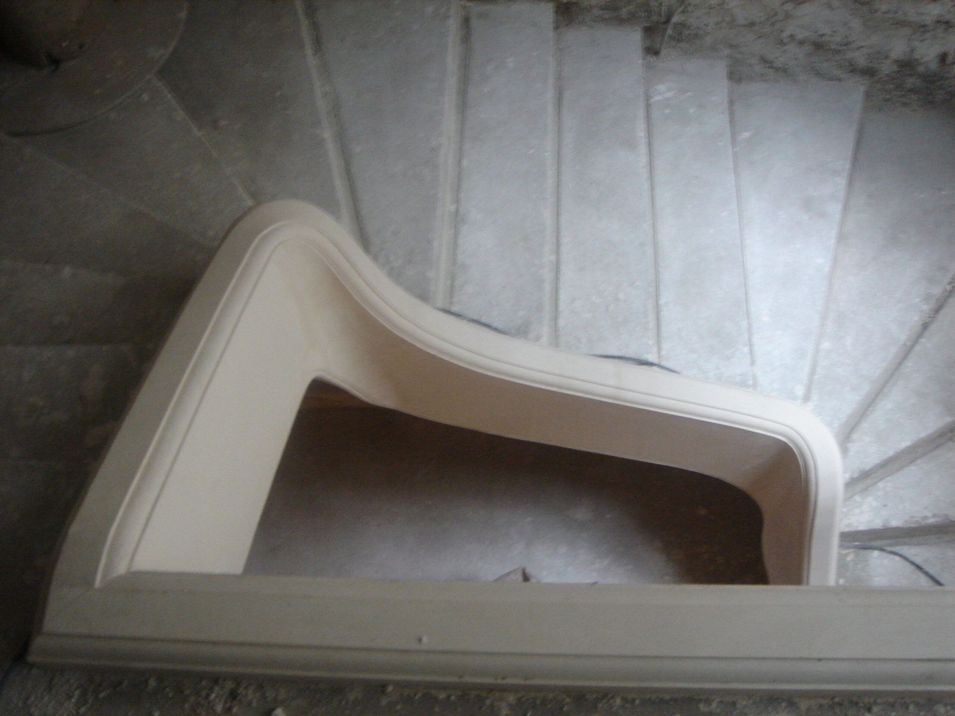 Vue de dessus d'un escalier incurvé en béton présentant une rampe lisse et de couleur claire.