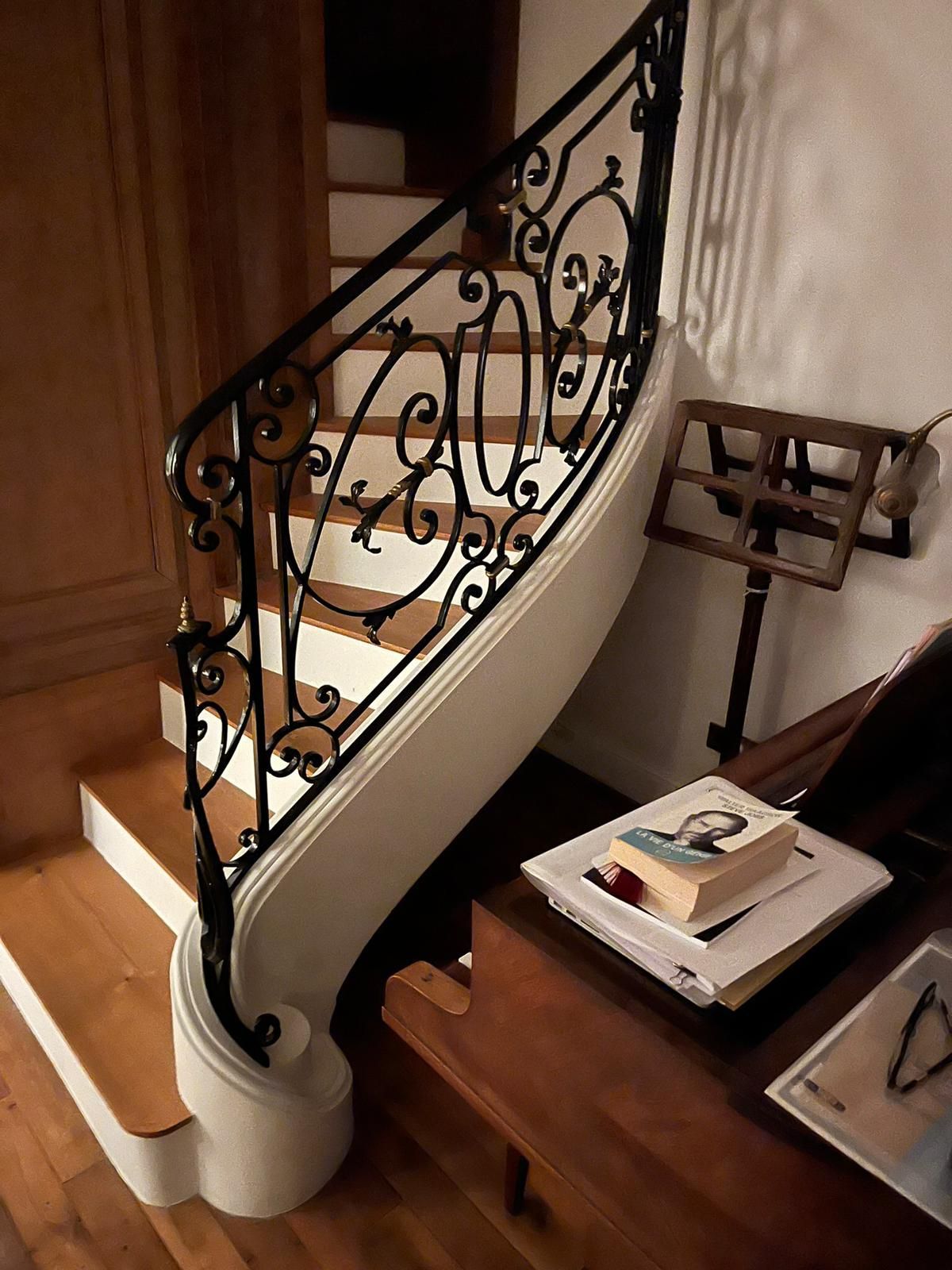 Un escalier en bois avec une rampe en métal se trouve à côté d'un pupitre et d'un piano sur lequel sont posés des livres.