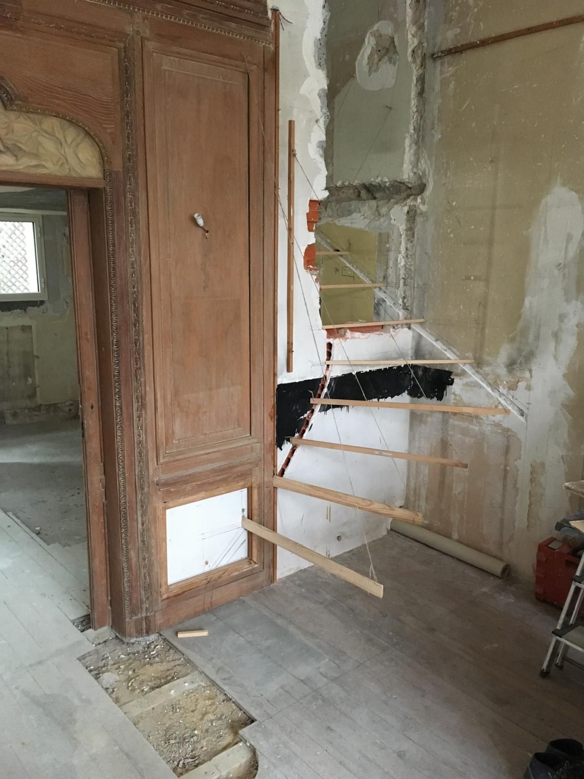 Une pièce en rénovation avec des briques apparentes, des lambris et de fausses marches en bois sur un mur.