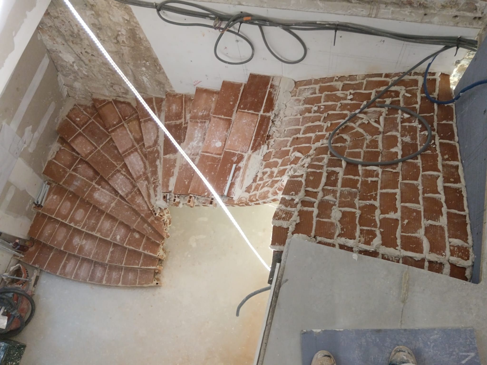 Vue en plongée d'un chantier de construction montrant un escalier dont les carreaux de terre cuite sont installés.