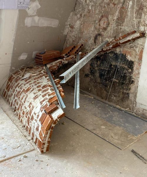 Une arche en briques inachevée et des poutres de soutien métalliques dans une pièce en construction.