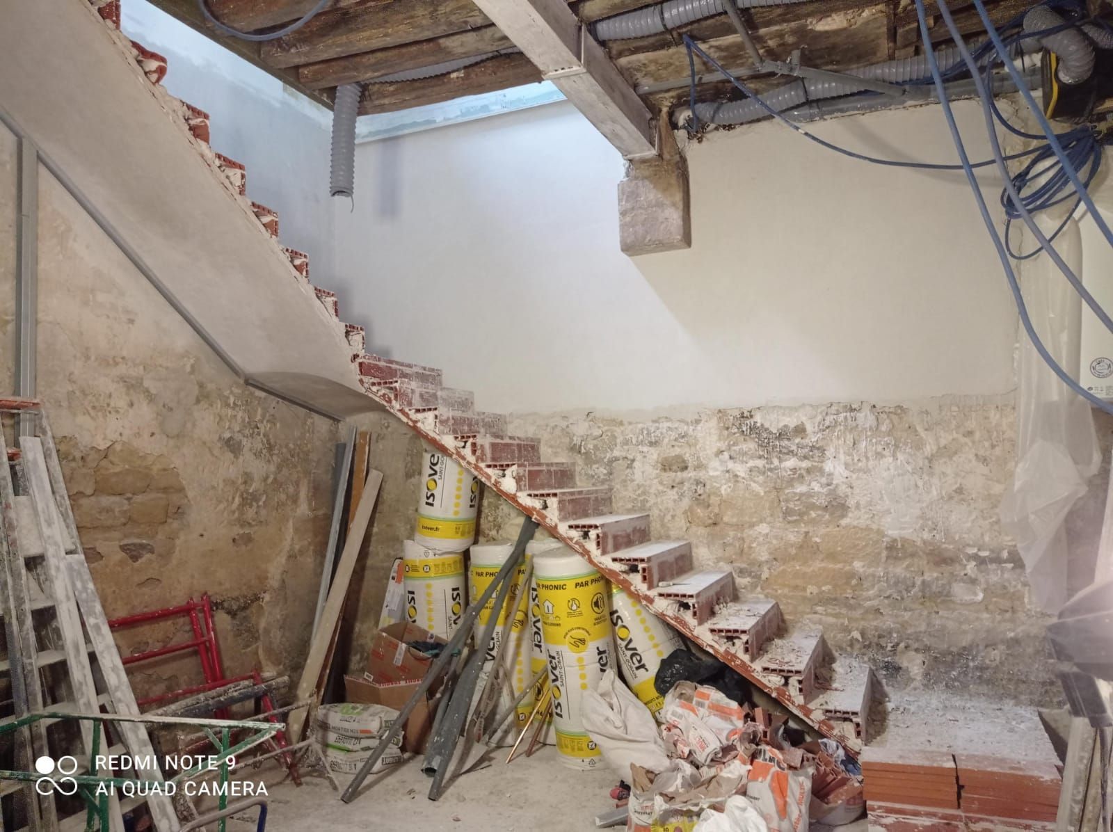 Escalier en rénovation avec des marches en briques apparentes, murs en pierres apparentes.