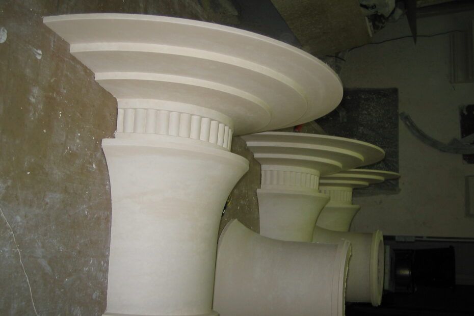 Dans un atelier, trois chapiteaux de colonnes inachevés, pâles et cannelés.