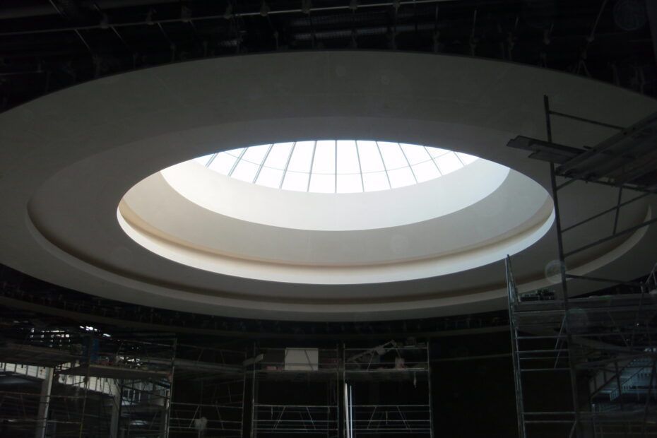 Une verrière circulaire et lumineuse intégrée à un plafond en dôme blanc, avec des échafaudages visibles en dessous.