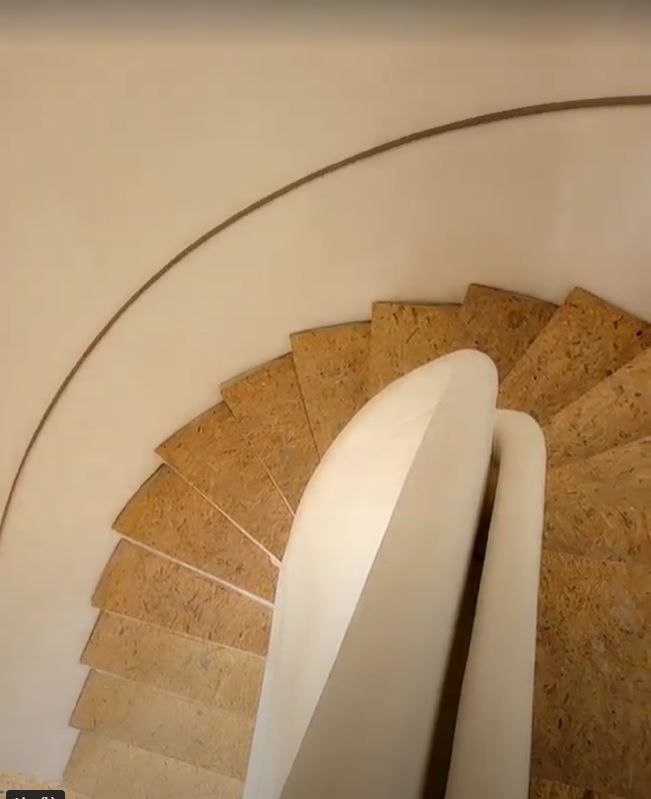 Vue de dessus d'un escalier en colimaçon aux marches texturées brun clair et à la rampe lisse et blanche incurvée.