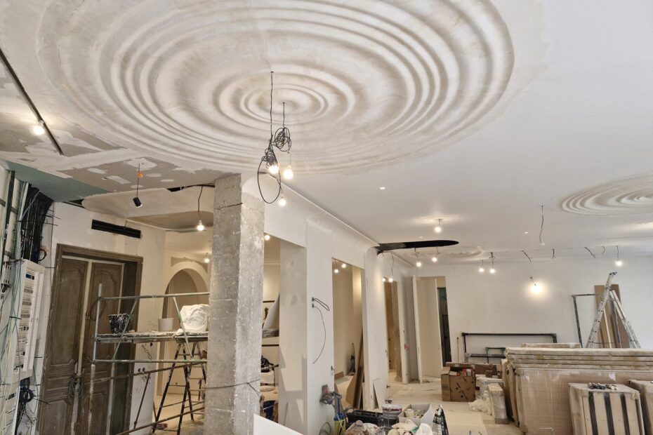 Chantier de construction avec des motifs circulaires au plafond, des luminaires suspendus et des murs bruts.