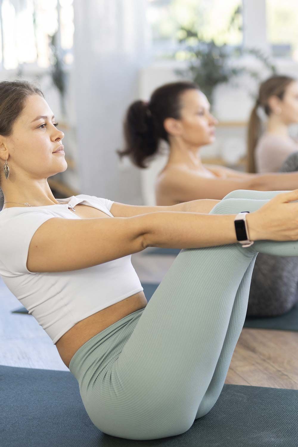 Mujer realizando un ejercicio de V-sit sobre una esterilla de yoga en un estudio luminoso.